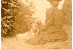 Nellie sitting on grass with dog. Nellie is facing away.