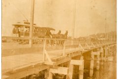 Horse and buggy passing an electric trolley on Astoria raised decked city street.